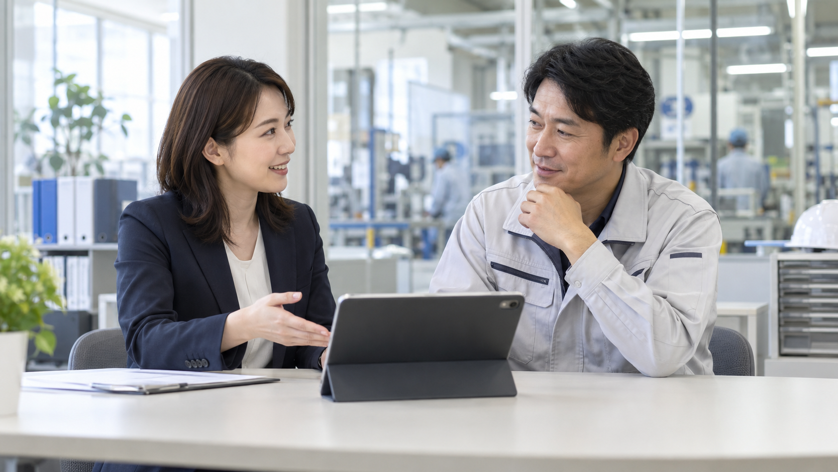 明るい製造業の事務スペースで人事担当者と現場責任者がタブレットを見ながら話し合う様子